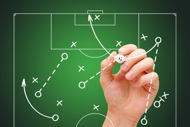 A hand drawing a tactical diagram on a picture of a football pitch.